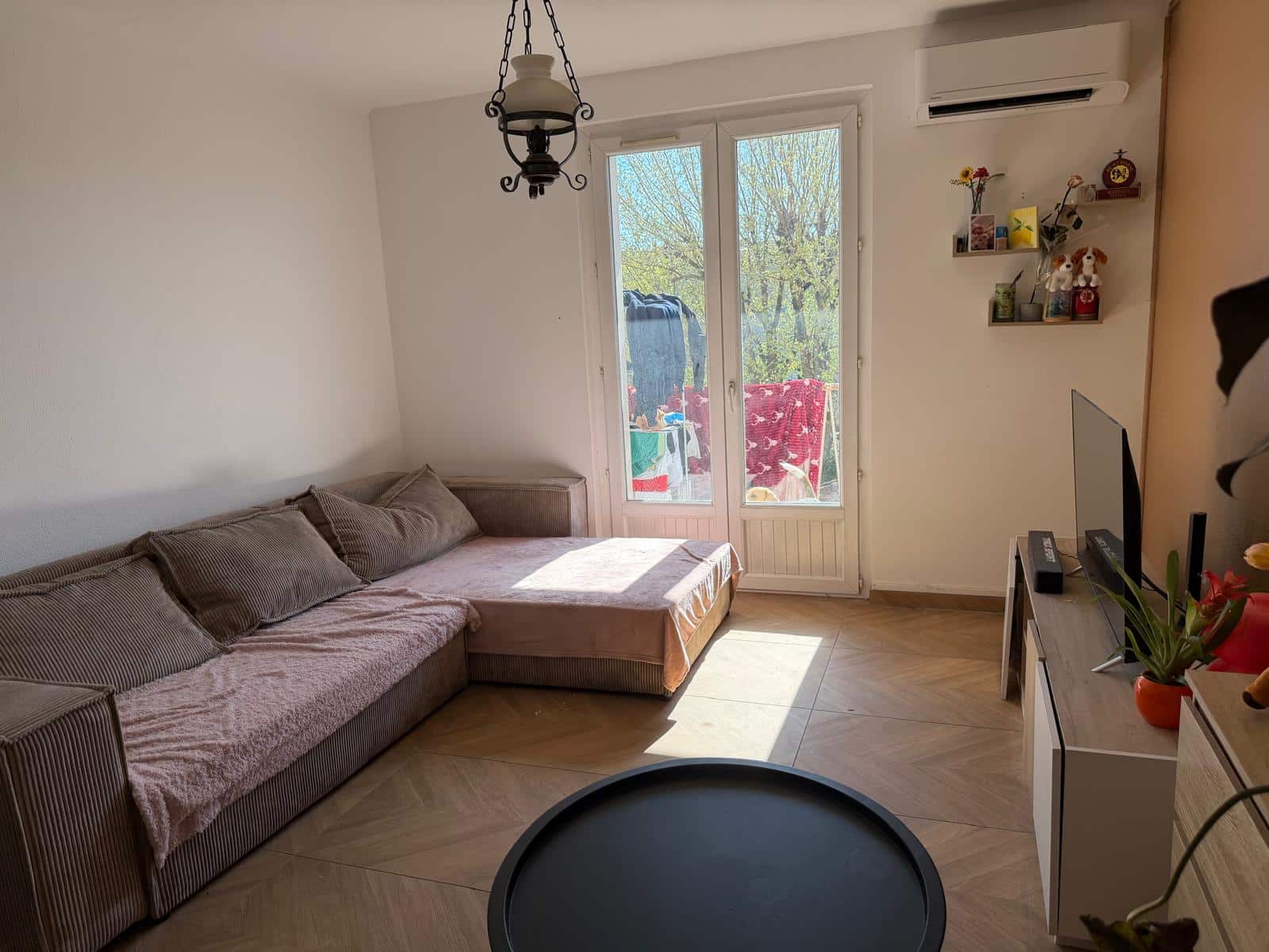 Living room with a striped sofa along the left wall, glass balcony door in the center, and a chandelier hanging from the ceiling.